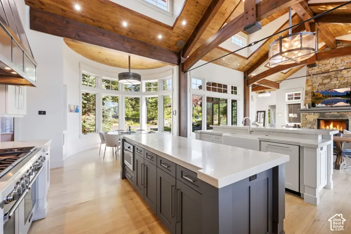 Exposed wood beam ceiling, expansive windows, multiple kitchen islands with stone countertops, integrated range with professional-grade hood, and a stone-clad fireplace
