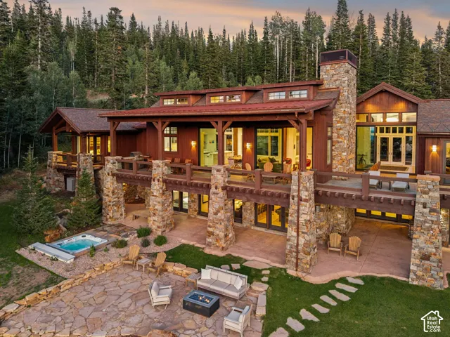 Timber-frame architecture with extensive stone masonry, multiple outdoor deck spaces, and a ground-level flagstone patio with a hot tub