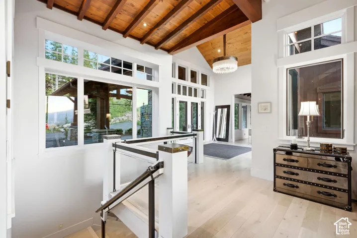 Vaulted wood plank and beam ceiling, light wood-finish flooring, white walls, and a contemporary chandelier
