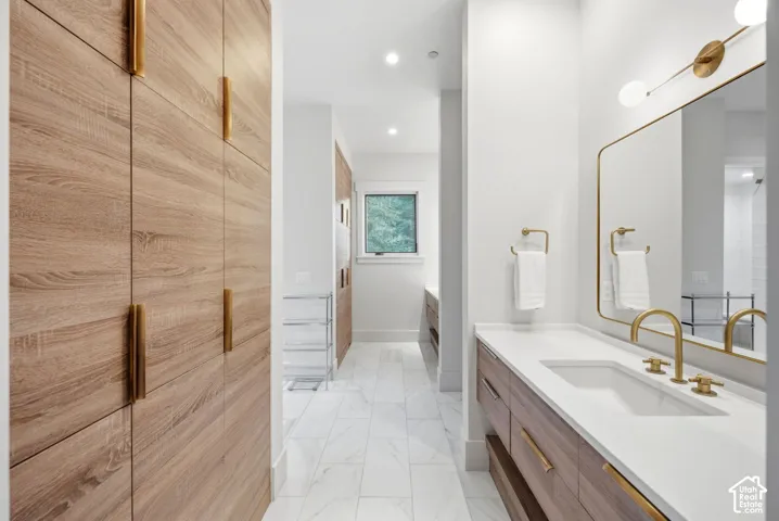 Wood-finish cabinetry with brass hardware, white countertop with an undermount sink, brass faucet, and large framed mirror