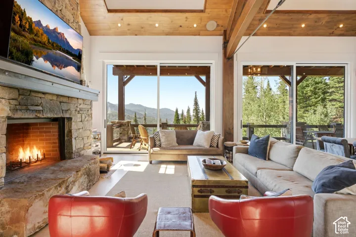 Stone fireplace with brick firebox, exposed wood beam ceiling, wood-finish flooring, and sliding glass doors leading to an outdoor deck
