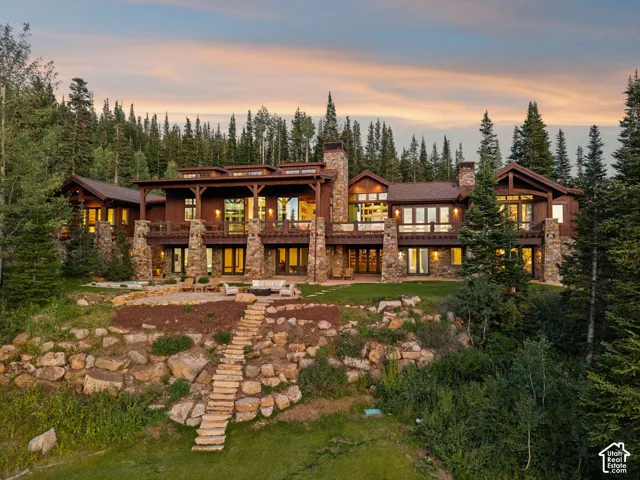 Multi-story residence featuring wood siding and stone accents, expansive windows, multiple balconies, a stone-paved patio, and a terraced stone pathway