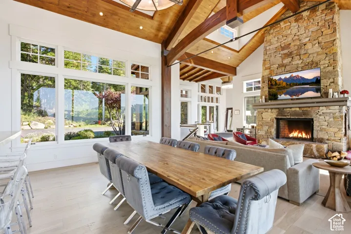 Vaulted wood-plank ceilings with exposed beams, expansive stone fireplace, light wood-finish flooring, and large picture windows