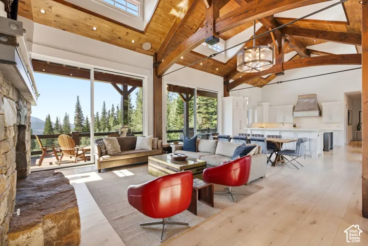 Great room with exposed wood beam vaulted ceilings, stone fireplace, wood-finish flooring, and a large sliding glass door leading to an outdoor deck
