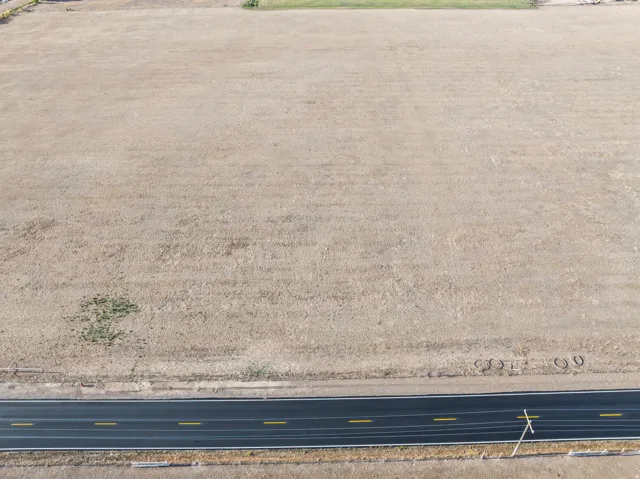 Expansive undeveloped land bordering a paved road with painted lane markings