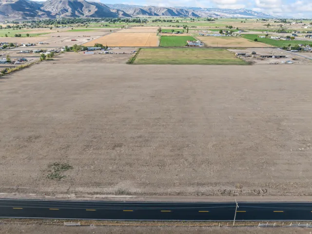 Expansive undeveloped land with a paved road frontage, surrounded by agricultural fields and distant mountains