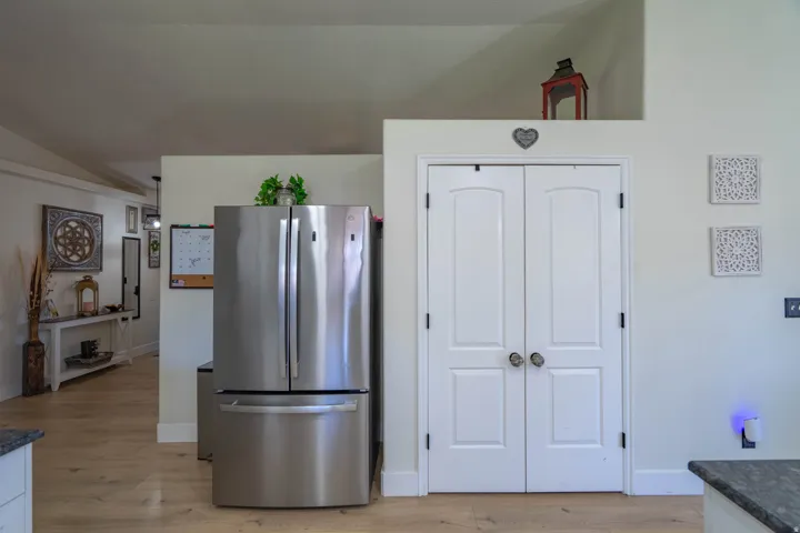 Stainless steel French door refrigerator, wood-finish flooring, white double doors with arched panels, and a granite-finish countertop