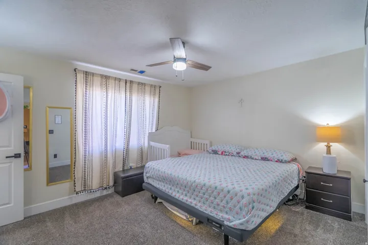 Spacious secondary bedroom featuring carpeted flooring, a ceiling fan with integrated lighting, and dual windows with vertical blinds providing natural light