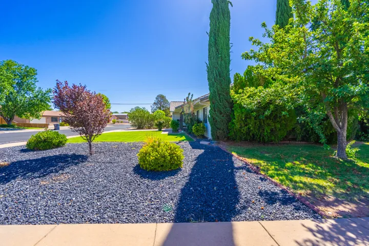 Landscaped front yard with black rock ground cover, diverse plantings, and mature trees