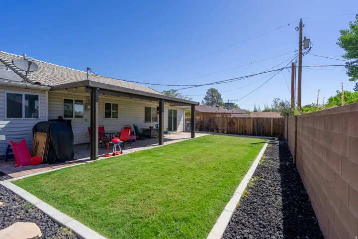 Expansive backyard featuring a covered patio, manicured lawn, and a block wall perimeter