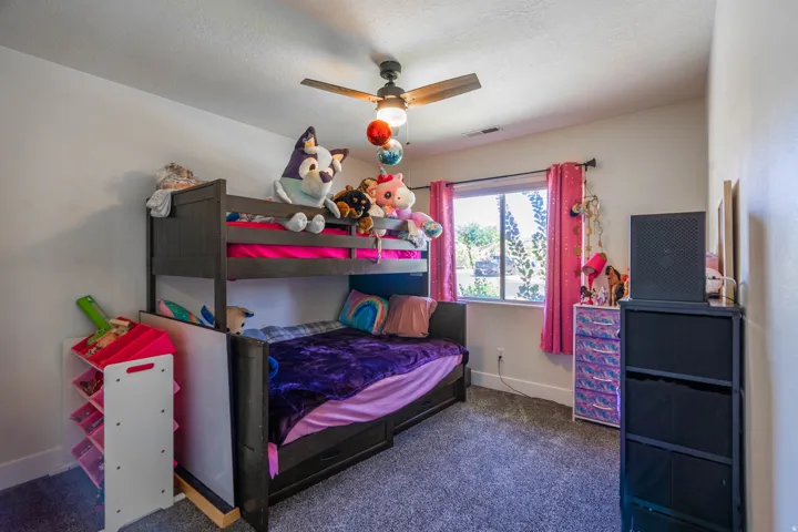 Carpeted bedroom featuring a bunk bed, a window with curtains, and a ceiling fan with integrated lighting