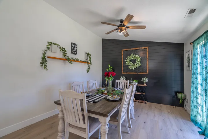 Dining room featuring a wood-finish table with turned legs, upholstered dining chairs, hardwood flooring, and a ceiling fan with integrated lighting