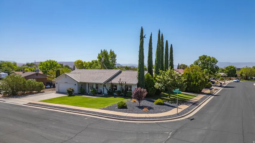 Corner-lot single-story residence featuring a pitched roof with composition shingles, stucco exterior, and mature Italian Cypress trees as striking focal points
