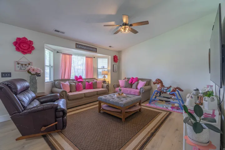 Bright, open living area featuring multiple seating zones with hardwood flooring anchored by a geometric-bordered area rug