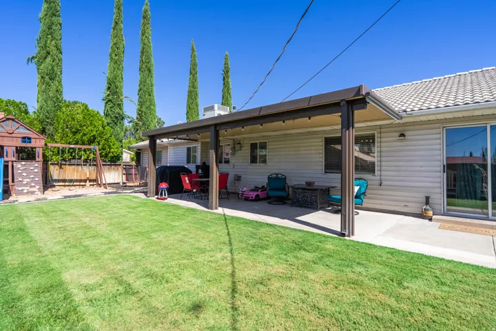 Expansive backyard oasis featuring a mature landscaped lawn, specimen Italian Cypress trees, and a covered patio with sturdy timber posts and metal roof