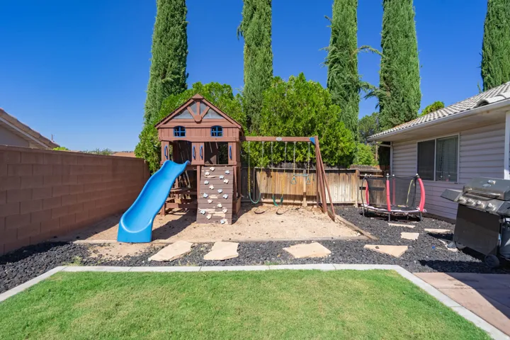 Backyard retreat featuring a manicured lawn, mature cypress trees, and a wood-frame play structure with integrated blue slide