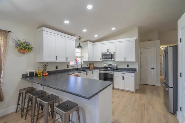 Spacious kitchen featuring an extended peninsula, white shaker-style cabinetry, dark countertops, and stainless steel appliances