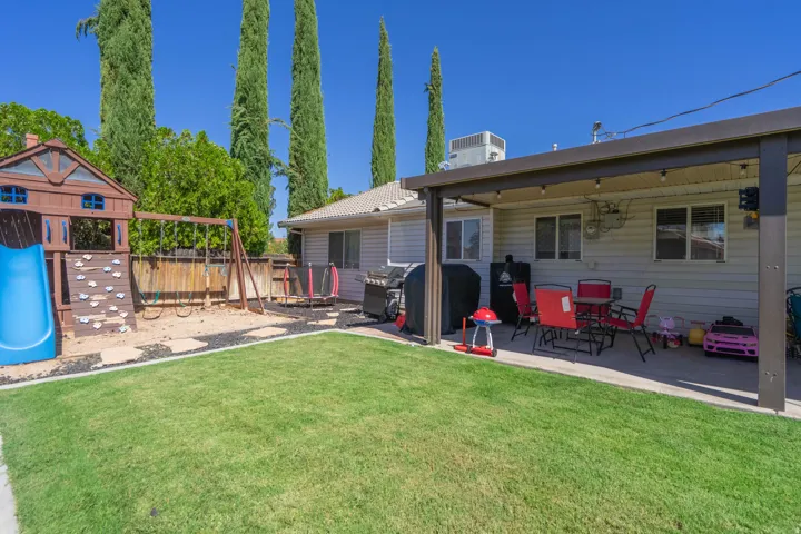 Expansive backyard oasis featuring a manicured lawn, mature Italian cypress trees, covered patio with red seating areas, detached storage shed with fencing, and a blue above-ground pool with surrounding decking—ideal for entertaining and outdoor recreat