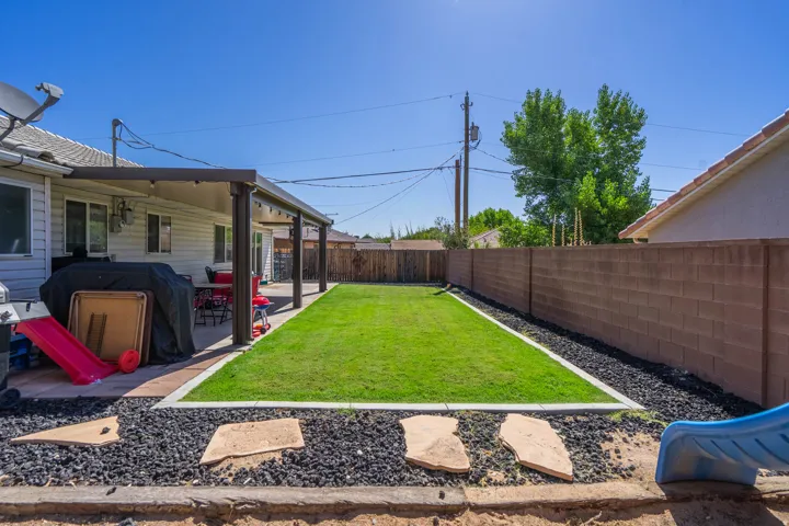 Expansive backyard featuring a newly installed synthetic turf lawn, decorative gravel borders with stepping stone pathway, mature shade trees, and privacy fencing