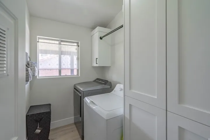 Dedicated laundry space featuring shaker-style cabinetry, a built-in hanging rod, and light wood-finish flooring