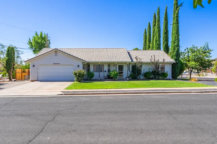 Charming single-story residence featuring a two-car garage, pitched tile roof, and mature landscape with Italian cypress trees