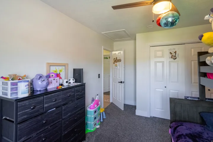 Spacious bedroom featuring carpet flooring, dual closets with white six-panel doors, black wood dresser with multiple drawers, ceiling fan with integrated lighting, and direct access to an ensuite bathroom