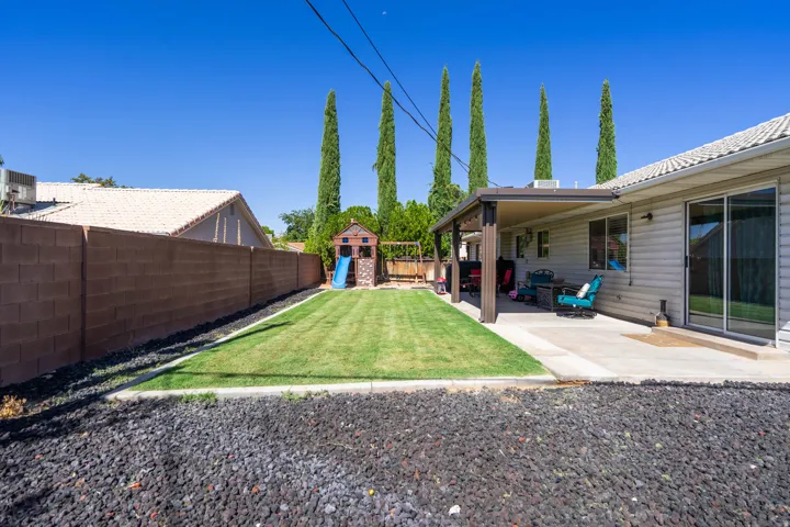 Expansive backyard featuring a covered patio, concrete block fence, manicured lawn, and sliding glass door access