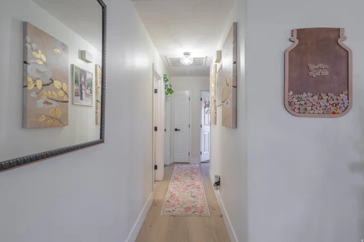 Recessed lighting illuminates a hallway with wood-finish flooring