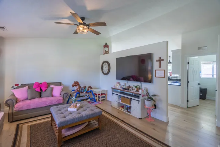 Bright, open-concept living area featuring hardwood flooring, a ceiling fan with integrated lighting, and a wall-mounted flat-screen television with built-in media shelving