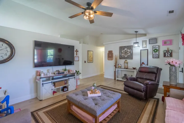 Vaulted ceiling with a ceiling fan, wall-mounted television, built-in entertainment console, and wood-finish flooring