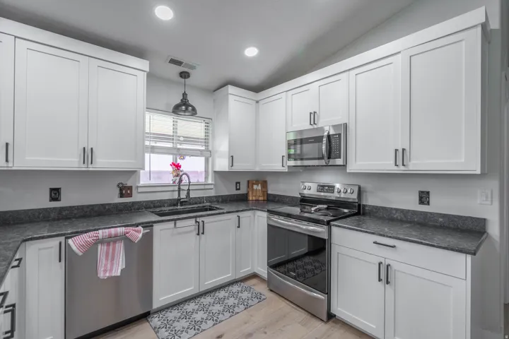 White shaker-style cabinetry with matte black hardware, dark stone-finish countertops, stainless steel appliances, and light wood-finish flooring