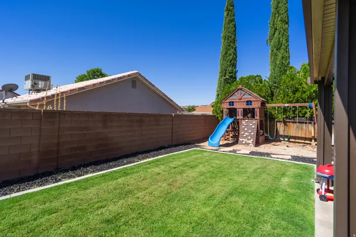 Expansive backyard featuring a manicured lawn, block wall fencing, and a covered patio area