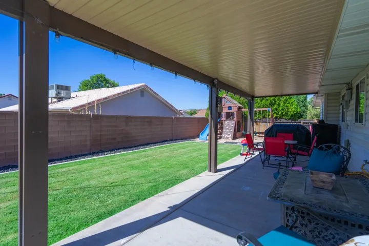 Covered patio with concrete flooring overlooking a spacious fenced backyard featuring mature landscaping and lush lawn