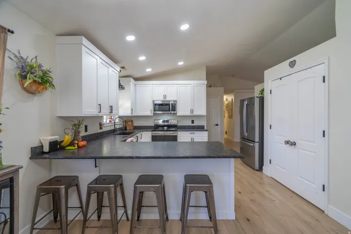 White shaker cabinetry with black hardware, dark stone countertops, stainless steel appliances, wood-finish flooring, and recessed lighting