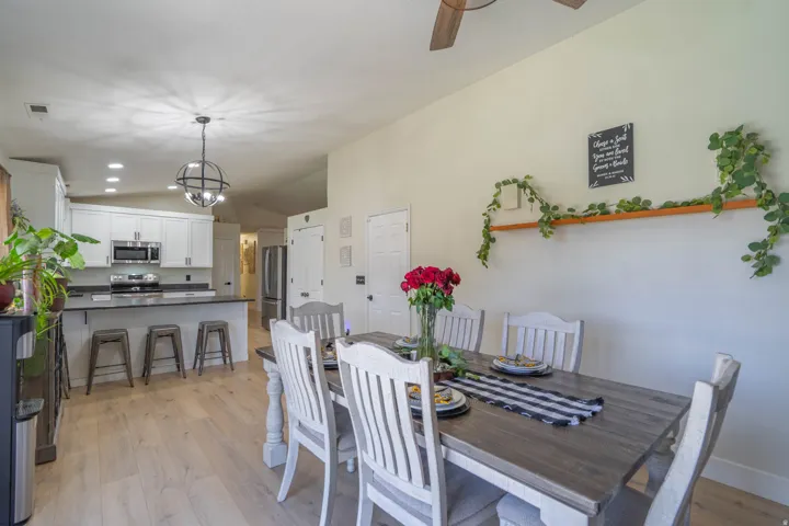 Open-concept living space featuring vaulted ceilings, wood-finish flooring, a kitchen island with dark countertops, white cabinetry, and stainless steel appliances