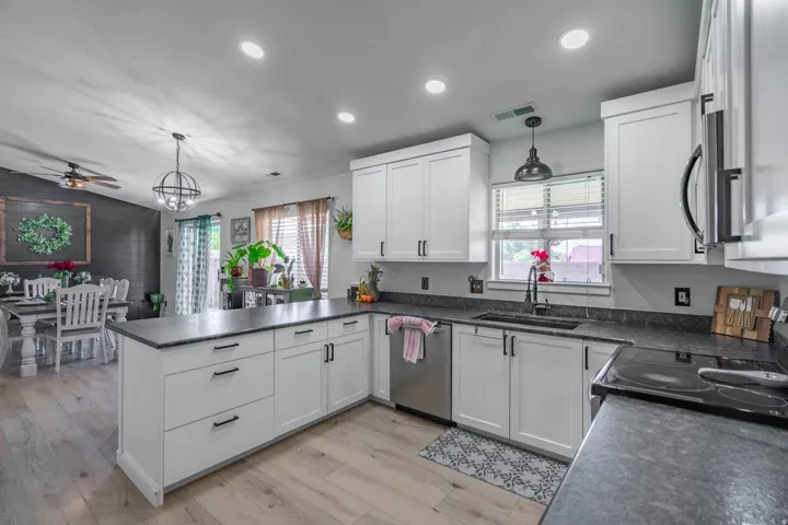 Modern kitchen featuring white shaker-style cabinetry with hardware accents, stainless steel appliances including a gas range and dishwasher, dark stone countertops, and a center island with seating