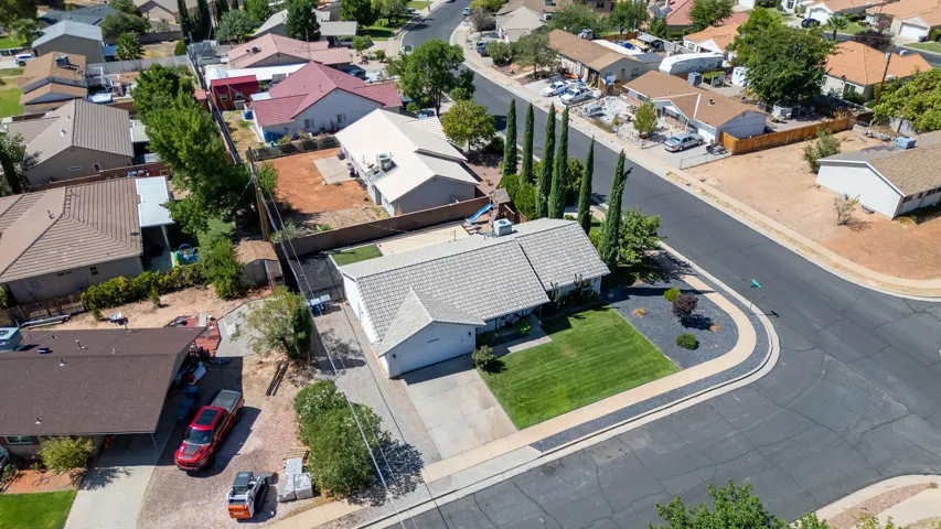Corner lot property featuring a light-colored shingle roof, attached garage, concrete driveway, and a manicured front lawn with mature landscaping