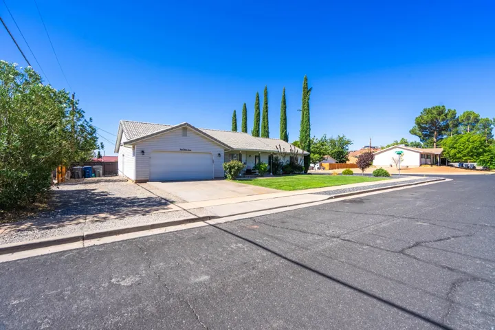 Charming single-story residence featuring a two-car garage, pitched roofline with neutral exterior finishes, and mature landscaping including distinctive Italian cypress trees
