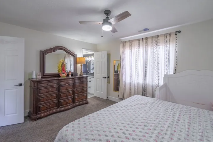 Spacious primary bedroom with carpet flooring, ceiling fan with integrated lighting, and a large dresser with mirror