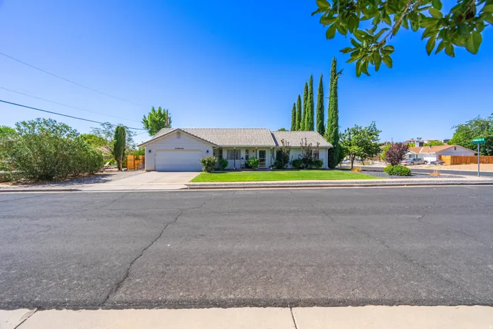Single-story residence featuring an attached garage, paved driveway, and a front lawn with mature landscaping