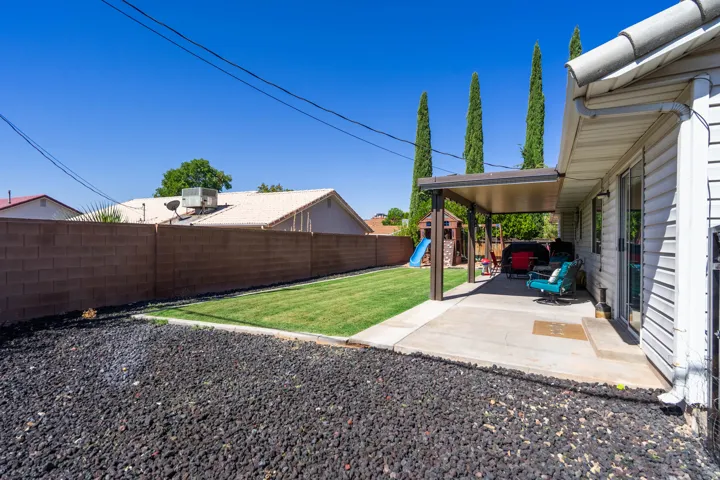 Spacious backyard oasis featuring a manicured lawn, mature cypress trees, and a covered patio with pergola structure