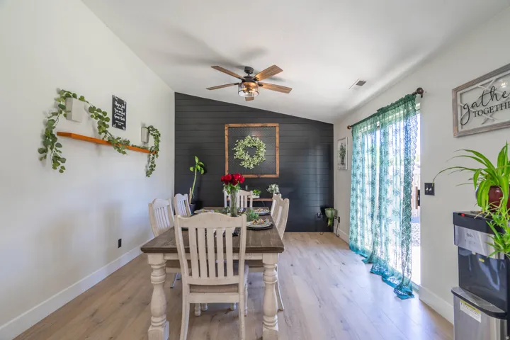 Wood-finish flooring, accent wall with horizontal paneling, ceiling fan with light fixture, and sliding glass door