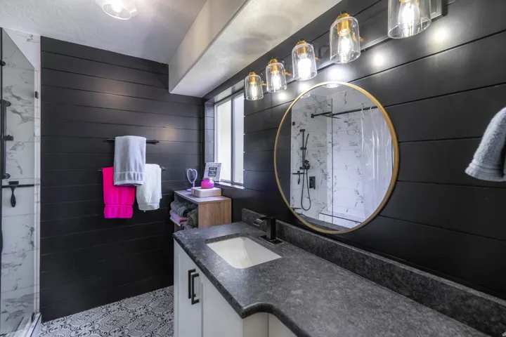Shiplap accent wall, custom vanity with integrated sink, black stone-finish countertop, walk-in shower with glass enclosure, and patterned floor tile
