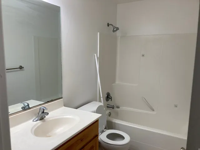 Bathroom featuring a wood-finish vanity with an integrated sink, a large wall-mounted mirror, and a shower-tub combination with a white surround