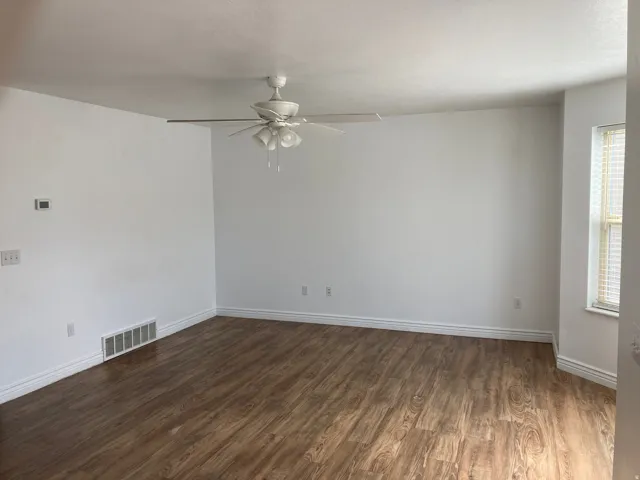 Spacious room featuring wood-finish flooring, white walls, and a ceiling fan