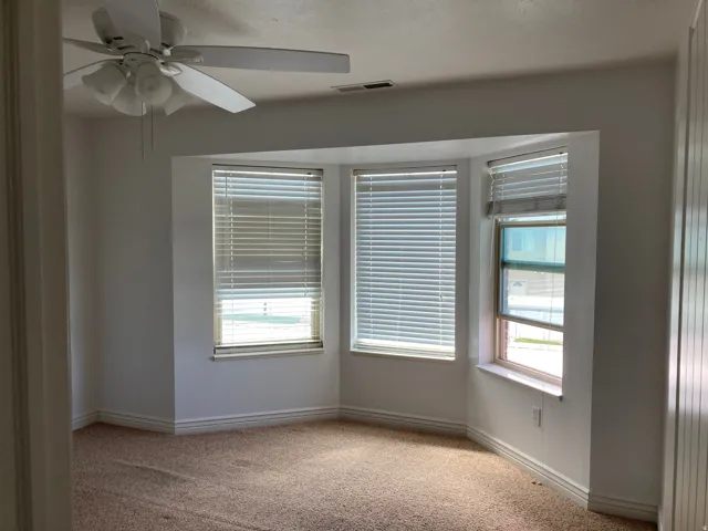 Room featuring a bay window, carpet flooring, a ceiling fan with integrated lighting, and vertical window blinds