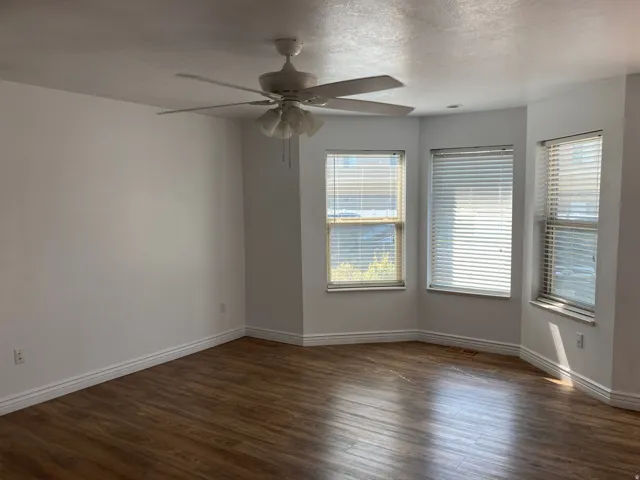 Bay window with three windows, wood-finish flooring, white walls, and a ceiling fan with integrated lighting