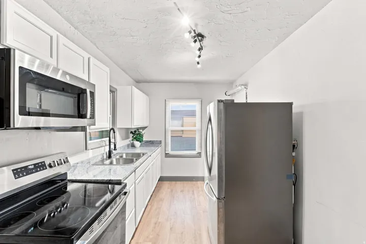 White cabinetry, stainless steel microwave, black electric range, double basin sink, and wood-finish flooring