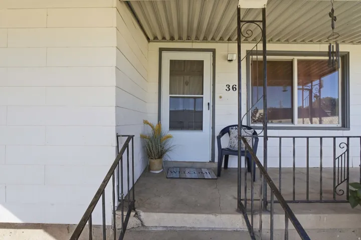 Covered front porch with a white entry door, an exterior window, and decorative wrought iron railings