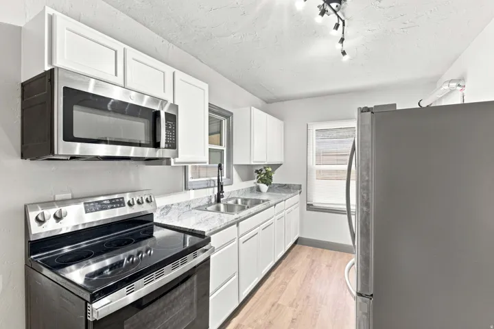 Kitchen featuring white cabinetry, stainless steel appliances, speckled countertops, a double basin sink, and wood-finish flooring